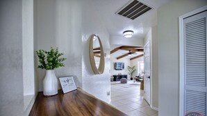 Um corredor com um banco de madeira, um vaso branco com plantas verdes e um espelho redondo na parede.