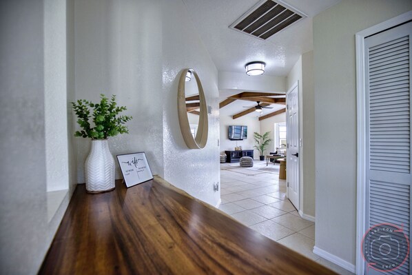 A hallway with a wooden bench, a white vase with green plants, and a round mirror on the wall.