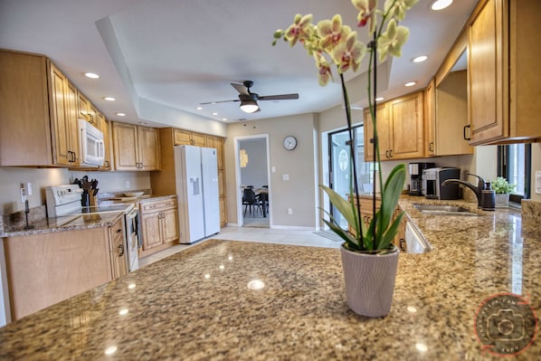 A kitchen with granite countertops, wooden cabinets, a ceiling fan, and a potted orchid.