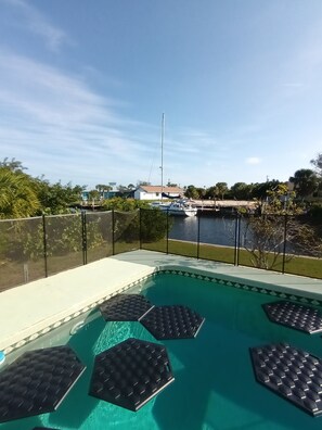 A swimming pool with hexagonal sun loungers, a view of a marina with boats, and a clear sky.