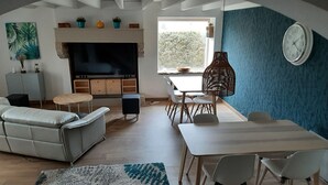 Ein Wohnzimmer mit Fernseher, einer Couch, einem Esstisch, Stühlen und einer blauen Akzentwand.