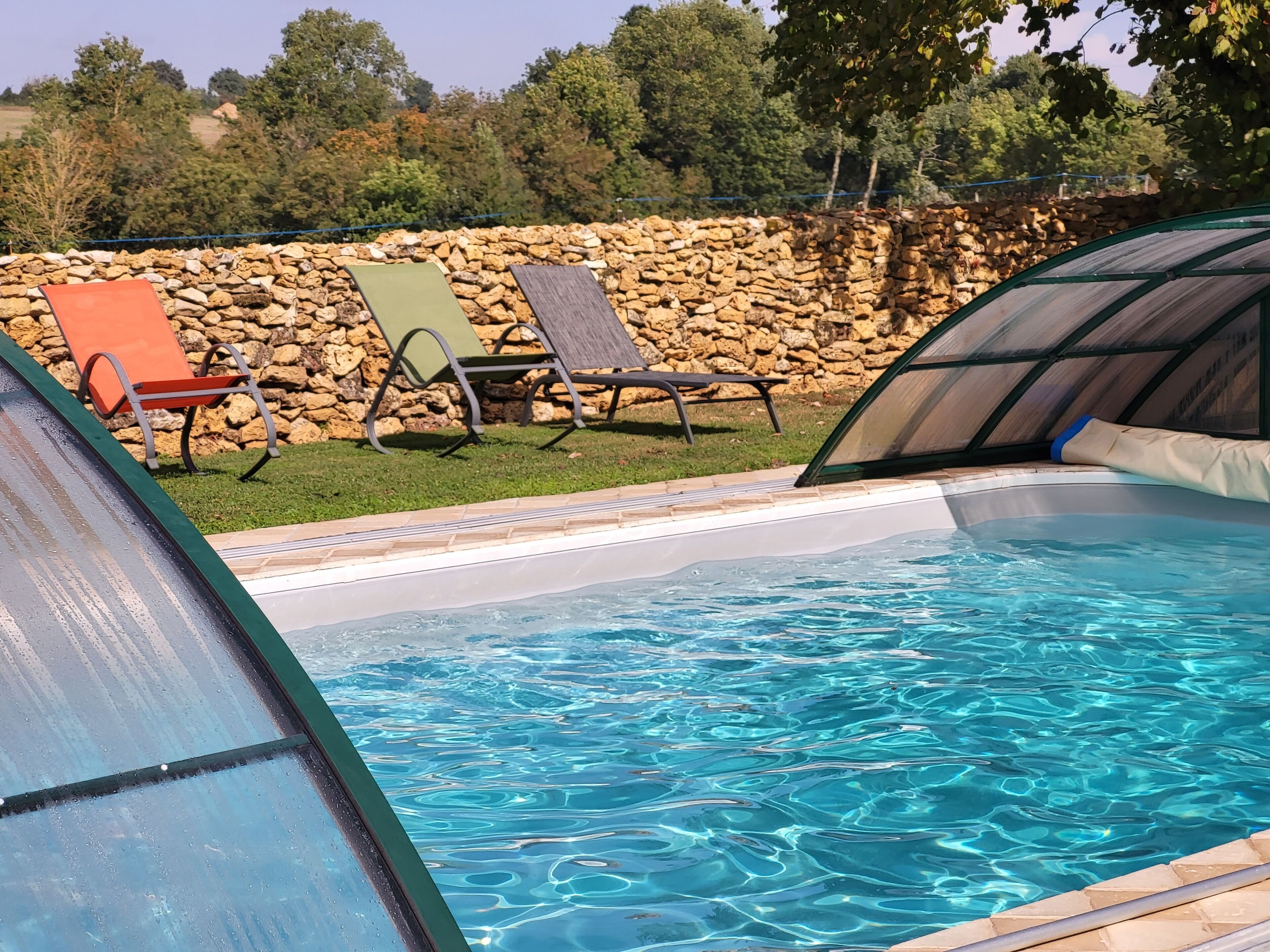 Piscina com água cristalina, rodeada por espreguiçadeiras e uma parede de pedra.
