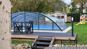 Ein Pool mit Glasveranda, Holzterrasse und einem kleinen Tisch mit Stühlen.