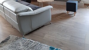 Ein modernes Wohnzimmer mit grauem Sofa, einem kleinen runden Tisch, einem Fernseher auf einem Steinkamin und einer Kommode mit Dekorationselementen.