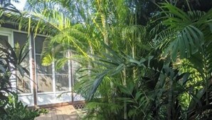 A patio with a round table and wicker chairs, surrounded by lush greenery and a glass enclosure. - Villa Valeria - An eco hideaway with all the modern luxuries (Cabo Rojo)