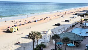 A beach with a pool area, umbrellas, and a lifeguard tower.