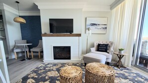 A modern living room with a fireplace, a television, a comfortable armchair, and a dining area with a small table and chairs.