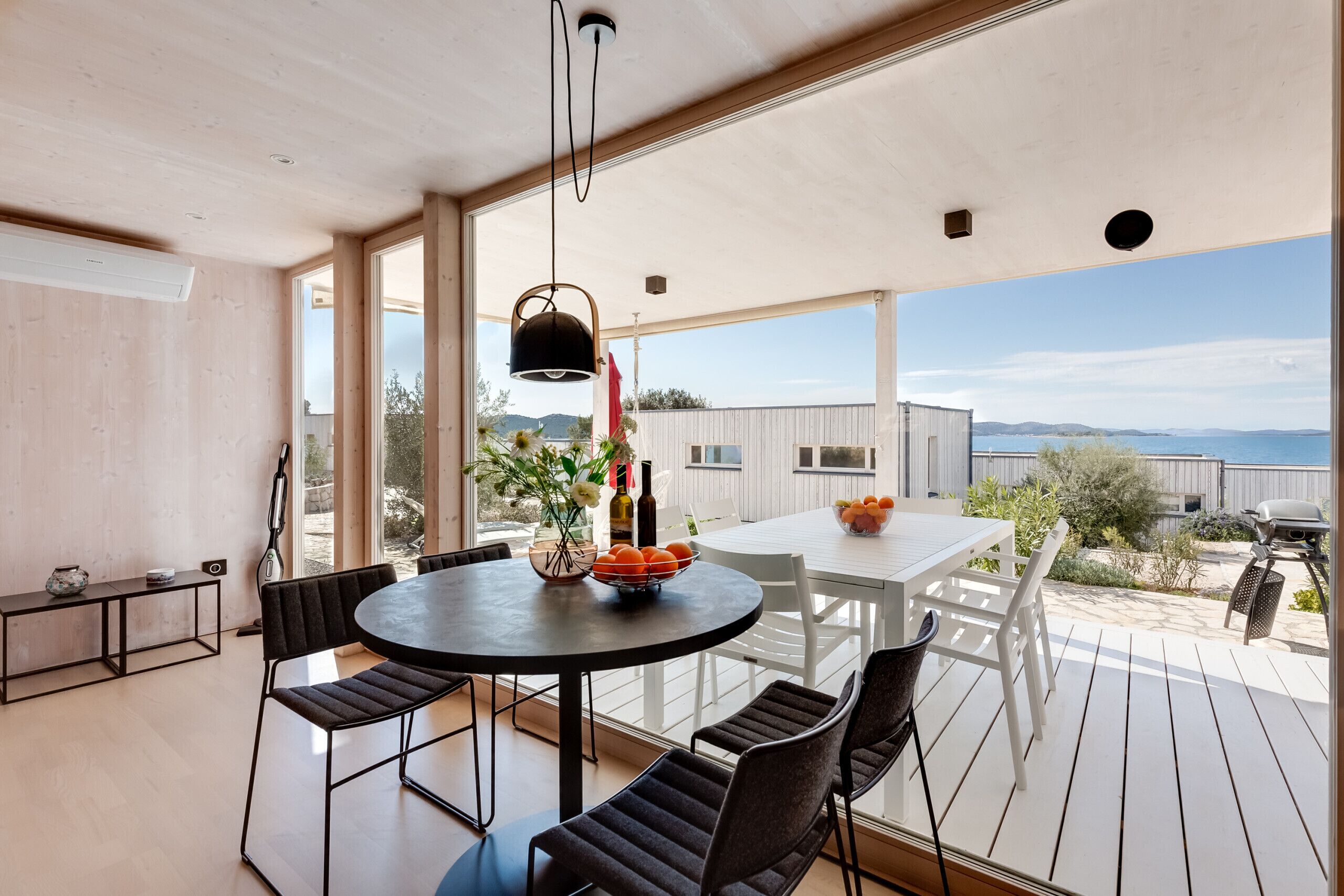 A modern dining area with a round table, black chairs, and a hanging light fixture.