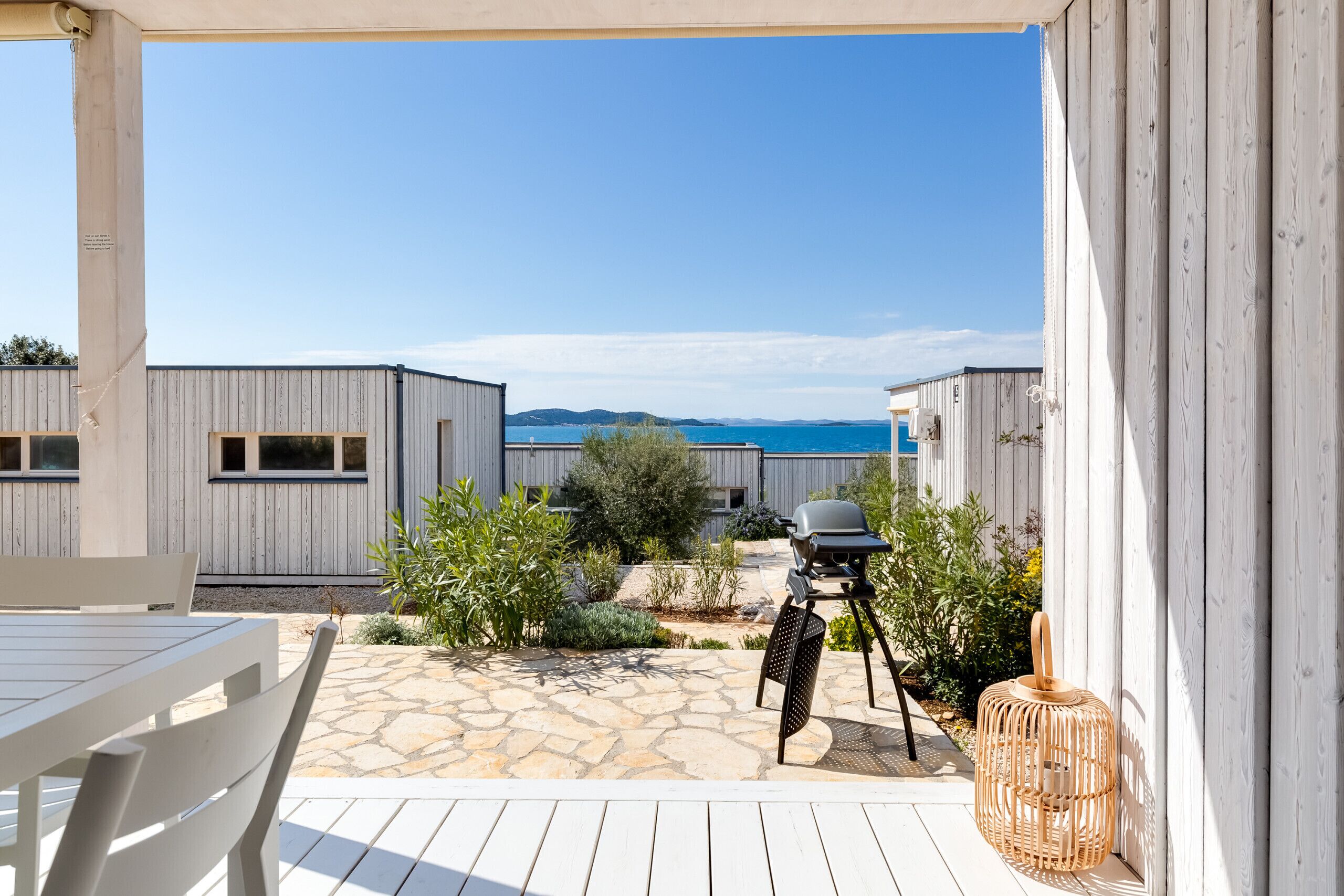 Un patio con suelo de piedra, mobiliario exterior, una parrilla y vista al mar.