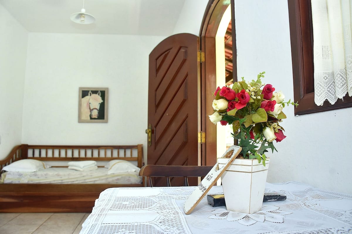 A bedroom with a wooden bed, a white bedside table, a vase with flowers, and a framed picture on the wall.