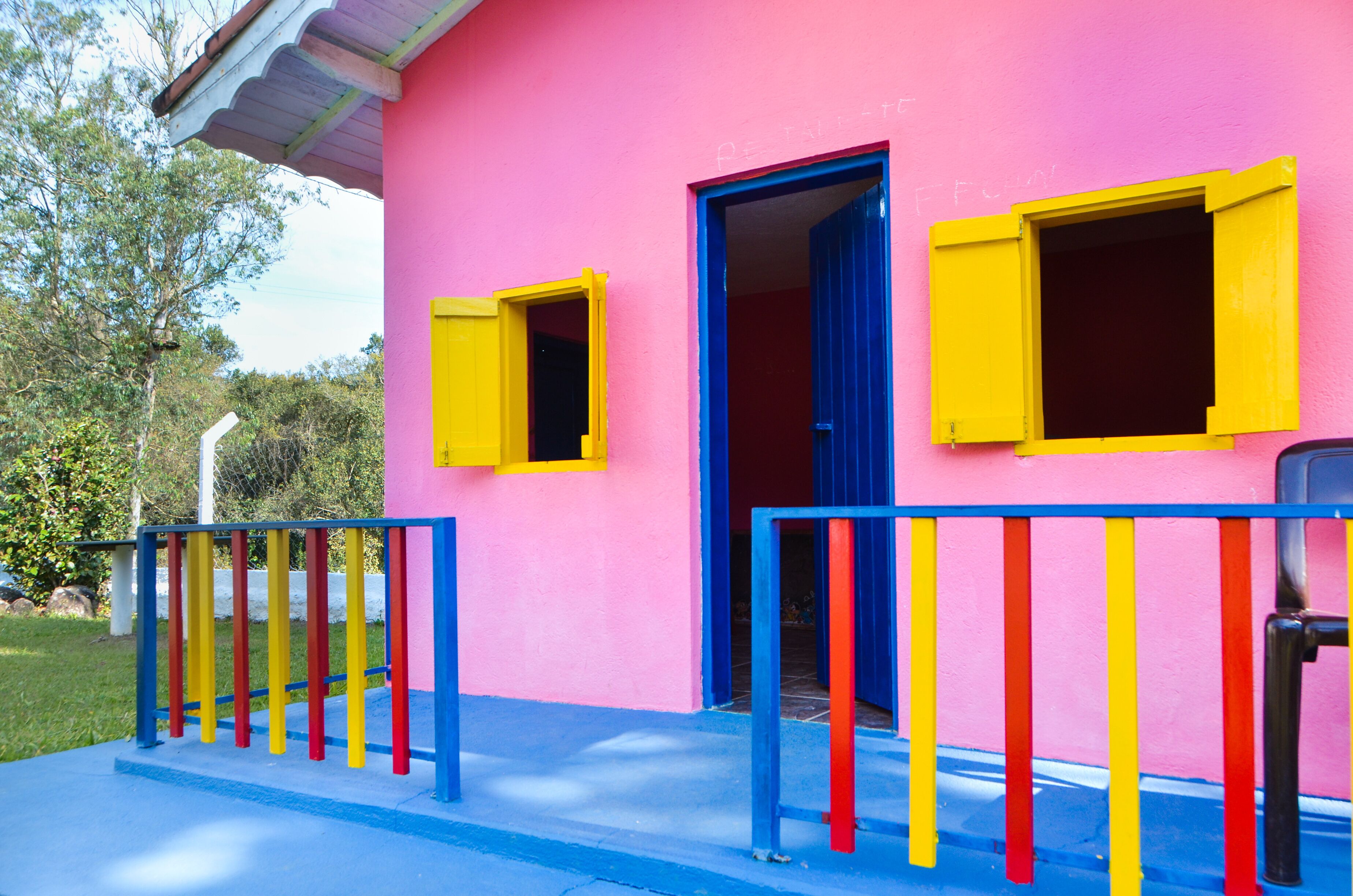 A pink building with yellow and blue shutters, a blue railing, and a door leading to an interior space.