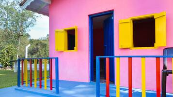 A pink building with yellow and blue shutters, a blue railing, and a door leading to an interior space.