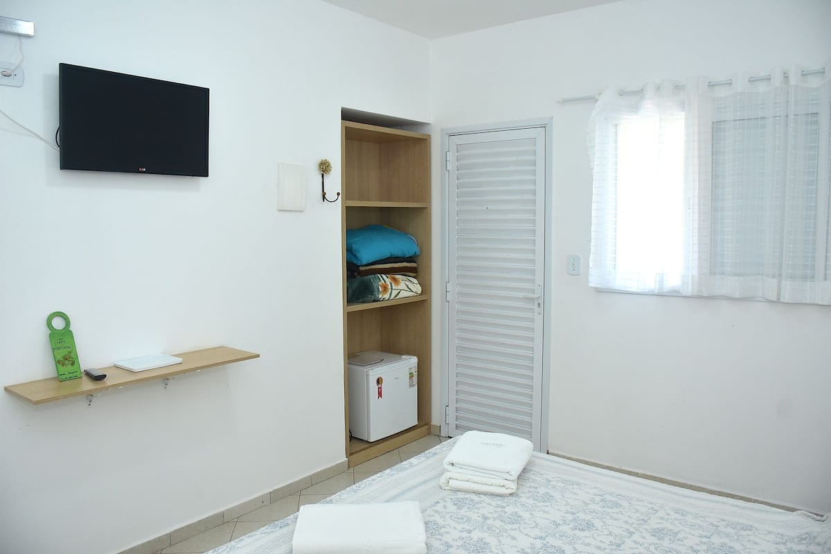A bedroom with a bed, a wardrobe, a shelf with a small appliance, and a television mounted on the wall.