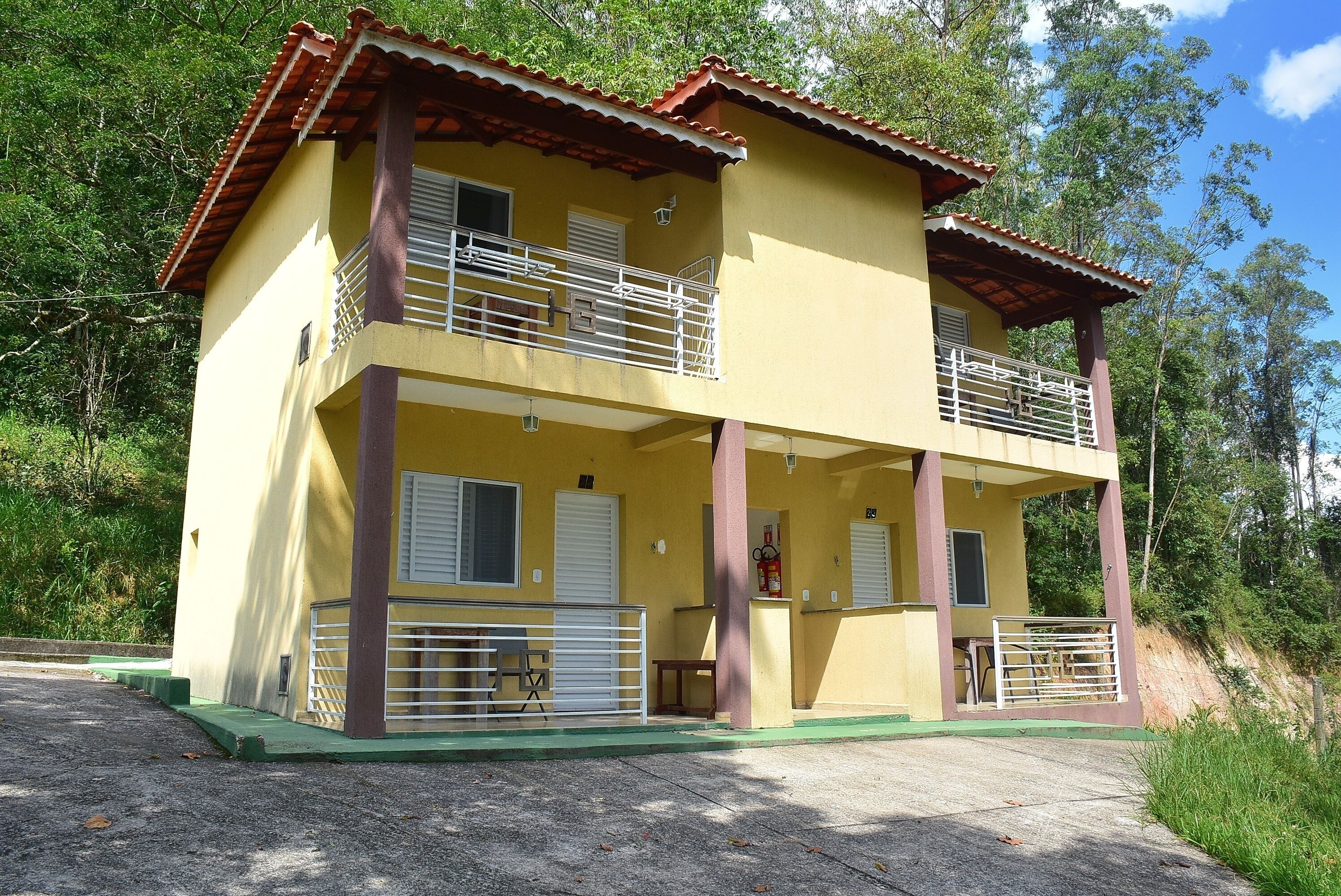 Un edificio amarillo de dos pisos con balcones, un extintor y un porche verde.