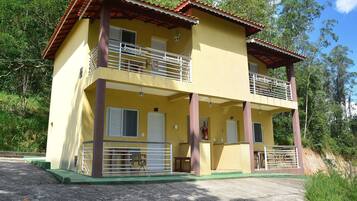 Un edificio amarillo de dos pisos con balcones, un extintor y un porche verde.