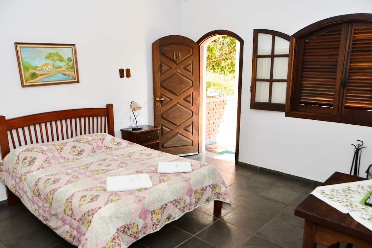 A bedroom with a bed, a wooden door, a window, and a painting on the wall.