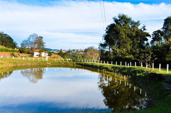 Um lago calmo com cerca branca e árvores refletidas na água.