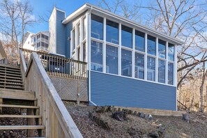 A modern house with large windows, a wooden deck, and a staircase leading to a balcony.