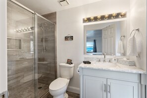 Un baño moderno con ducha de vidrio, inodoro blanco y tocador con espejo e iluminación.