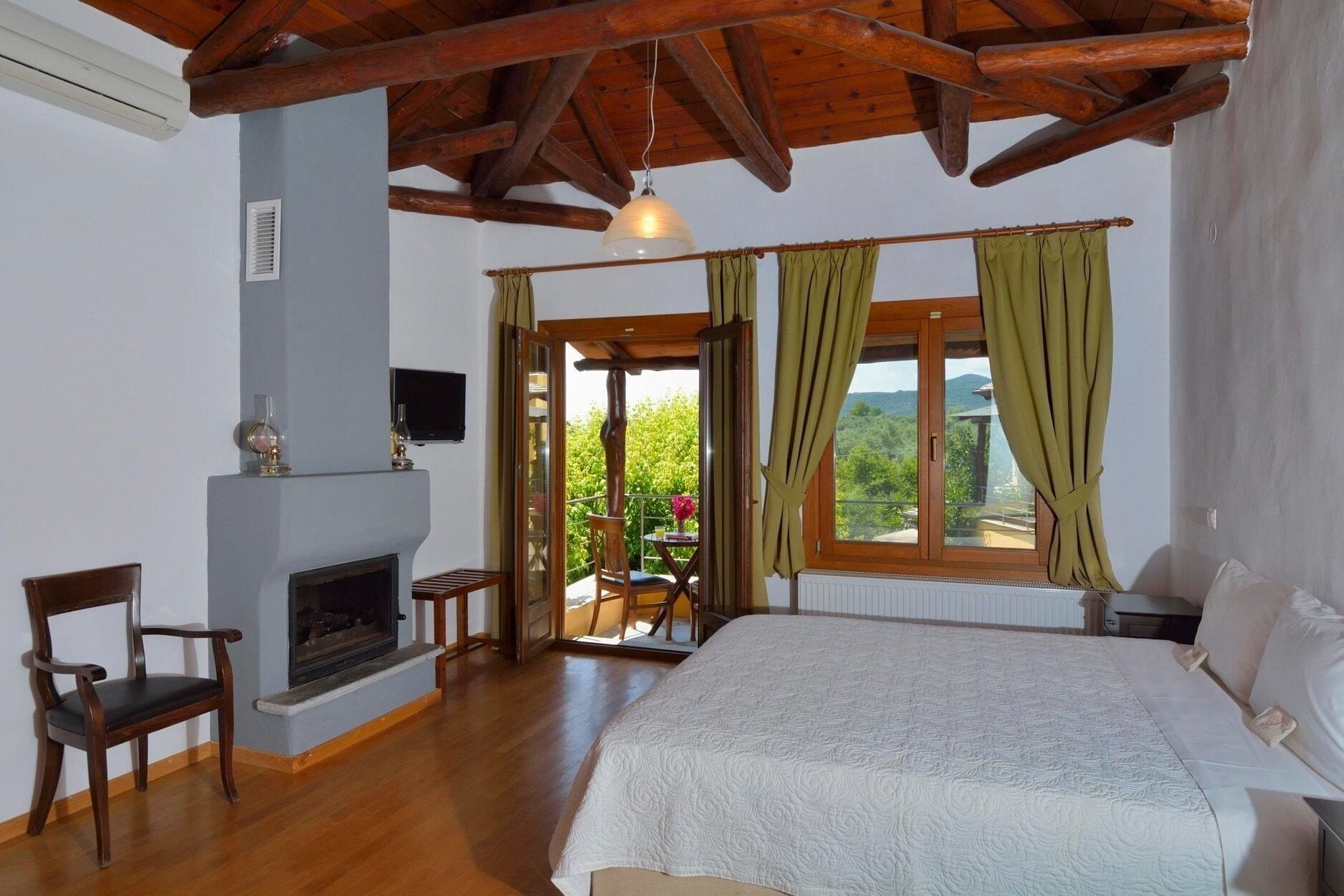 A bedroom with a fireplace, a bed, a window with curtains, and a view of greenery outside.