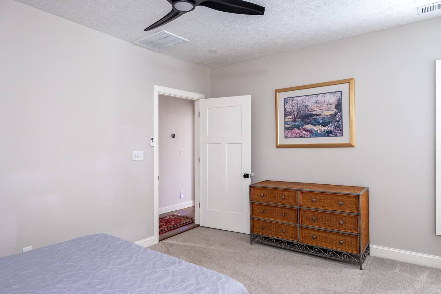 A bedroom with a bed, a dresser, a ceiling fan, a door, and a framed picture on the wall.