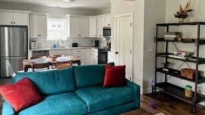 Eine moderne Küche mit weißen Schränken, einem Edelstahlkühlschrank und einem Essbereich mit einem blaugrünen Sofa und roten Kissen.