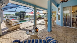 A covered outdoor area with a pool, wicker furniture, and a table with a lantern.