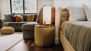 A cozy bedroom with a bed, a nightstand with a lamp, a sofa, and a round ottoman.