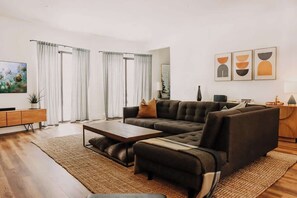 Un salon moderne avec un canapé d’angle, une table basse et une grande fenêtre agrémentée de rideaux.