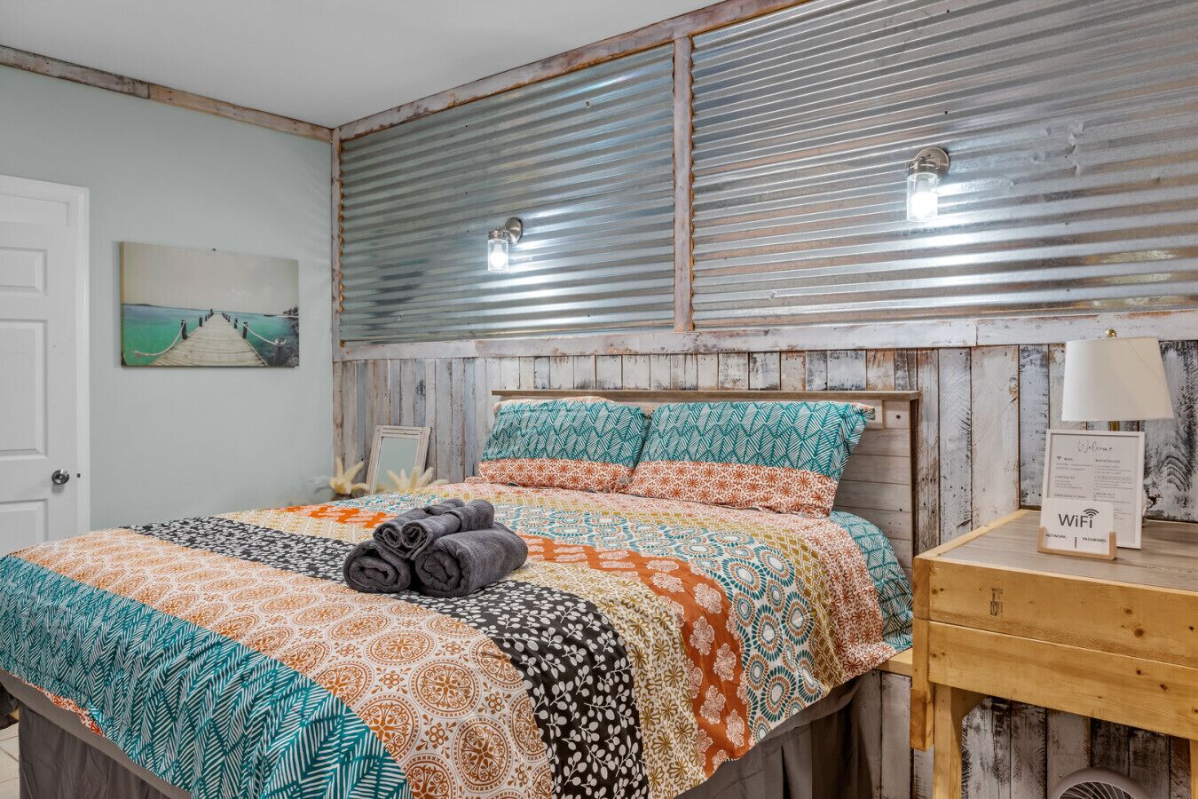 Une chambre à coucher avec un lit, une table de chevet en bois, une lampe fixée au mur et une porte.
