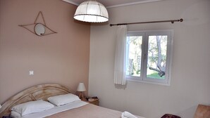 A neatly made bed with white linens, a bedside lamp, and a window with curtains. - Seawave Villa (Καραβαδος)