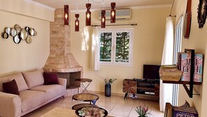 A living room with a beige sofa, a coffee table, a fireplace, and a bookshelf. - Seawave Villa (Καραβαδος)