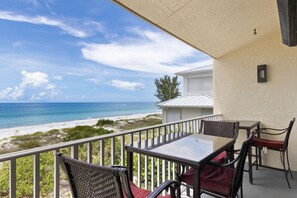 En balkon med et bord og stole, der ud til en strand og et hav.