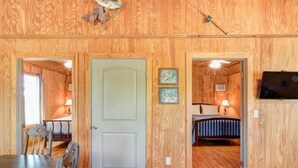 A wooden interior with a dining area, a bedroom with a bed and nightstand, and a television mounted on the wall. - Gone Fishin` Cabin at Lightning Bug Springs (Uvalde)