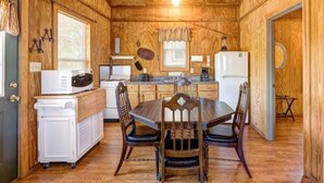 A compact kitchen with wooden walls, a dining table, chairs, a refrigerator, a microwave, and a sink. - Gone Fishin` Cabin at Lightning Bug Springs (Uvalde)