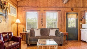 A cozy cabin interior with a wooden ceiling, a brown sofa, a red leather chair, and a glass coffee table. - Gone Fishin` Cabin at Lightning Bug Springs (Uvalde)