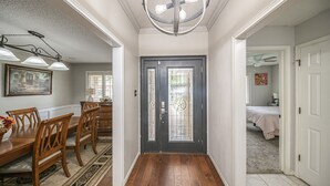 Un couloir doté d’un plancher en bois, une porte noire ornée de panneaux de verre décoratifs et un coin repas avec une table et des chaises en bois.