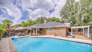 Un jardin avec une piscine, une maison en briques et un patio couvert.