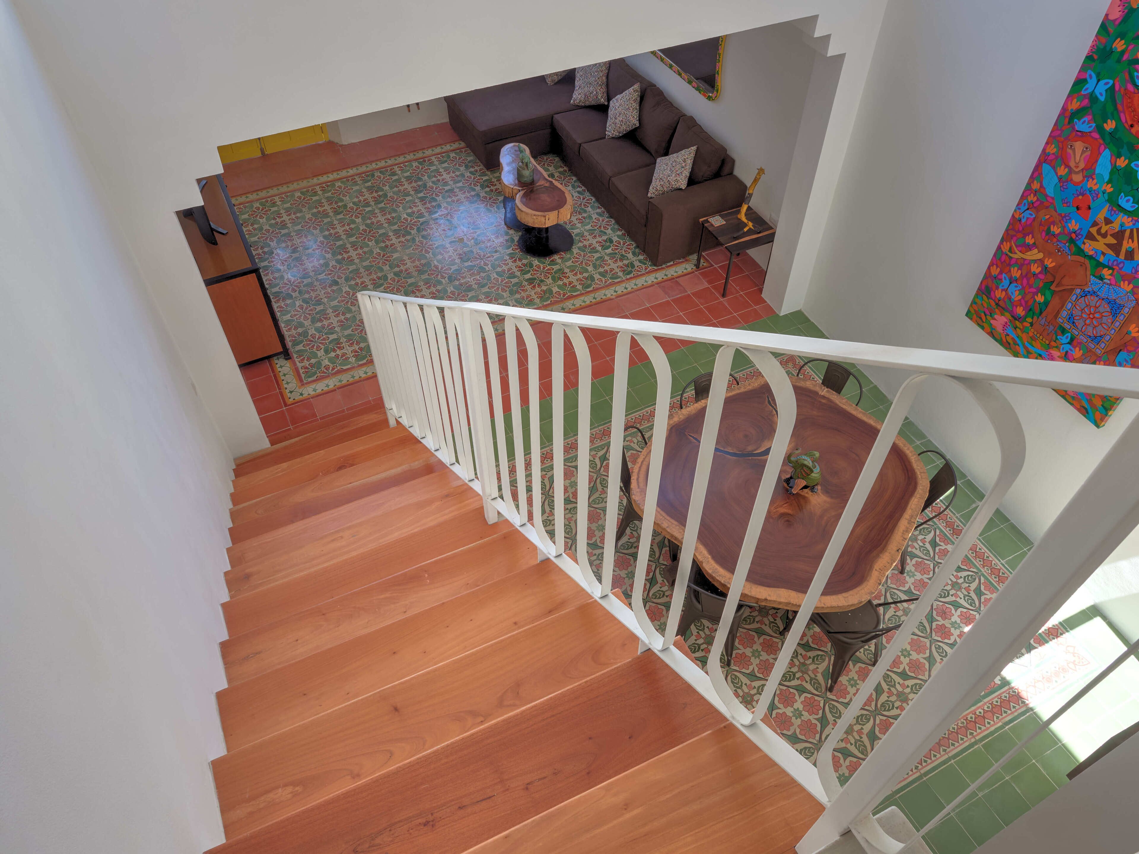 Eine Holztreppe mit weißer Geländer führt zu einem Wohnbereich mit braunem Sofa, einem gemusterten Teppich und einem runden Holztisch.