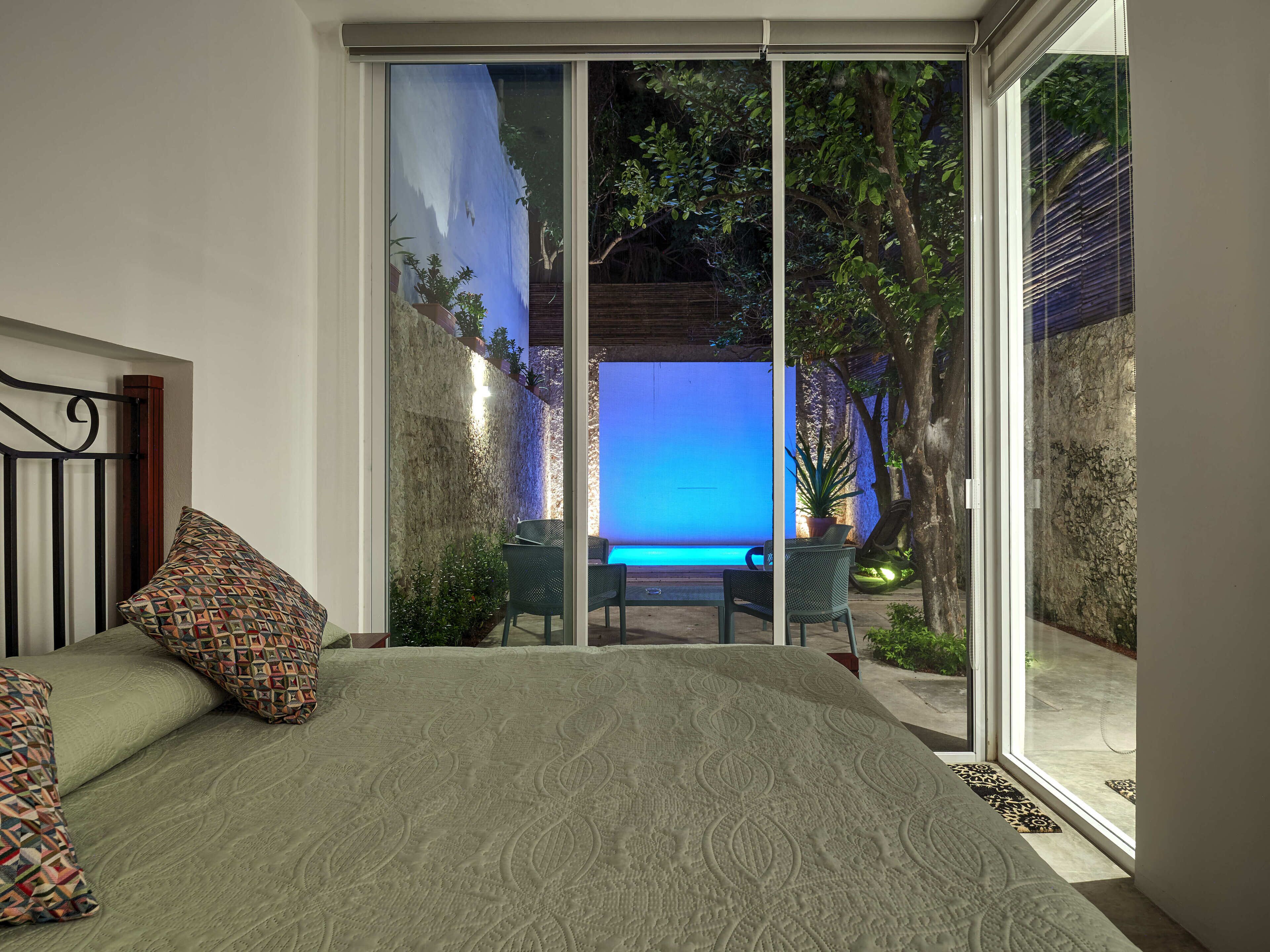 A bedroom with a large bed, a view of an outdoor pool, and a sliding glass door leading to a patio area.