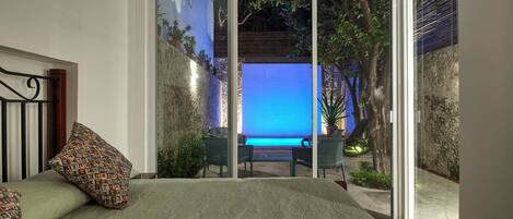 A bedroom with a large bed, a view of an outdoor pool, and a sliding glass door leading to a patio area.