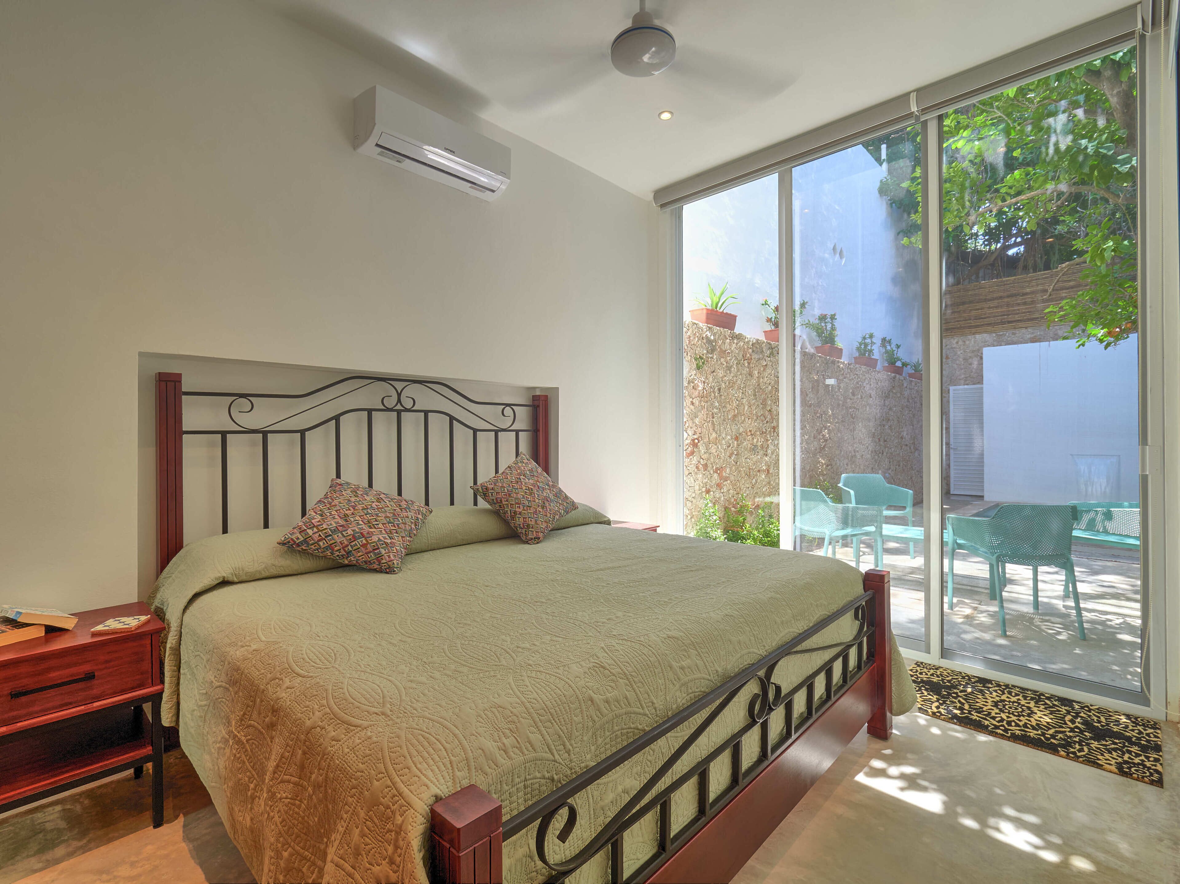 A bedroom with a bed, a nightstand, a window, and a view of the outside.