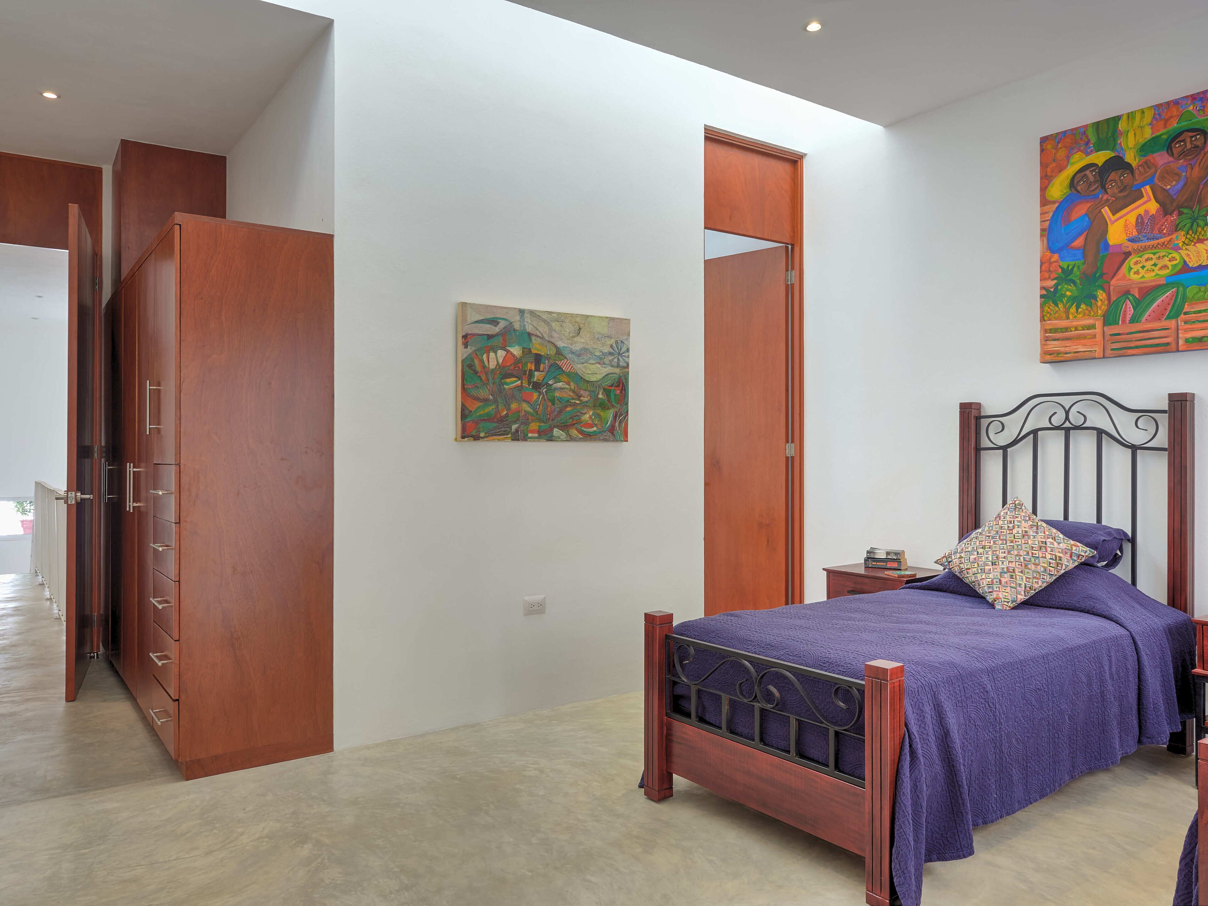 A bedroom with a wooden wardrobe, a bed with a purple bedspread, and a painting on the wall.
