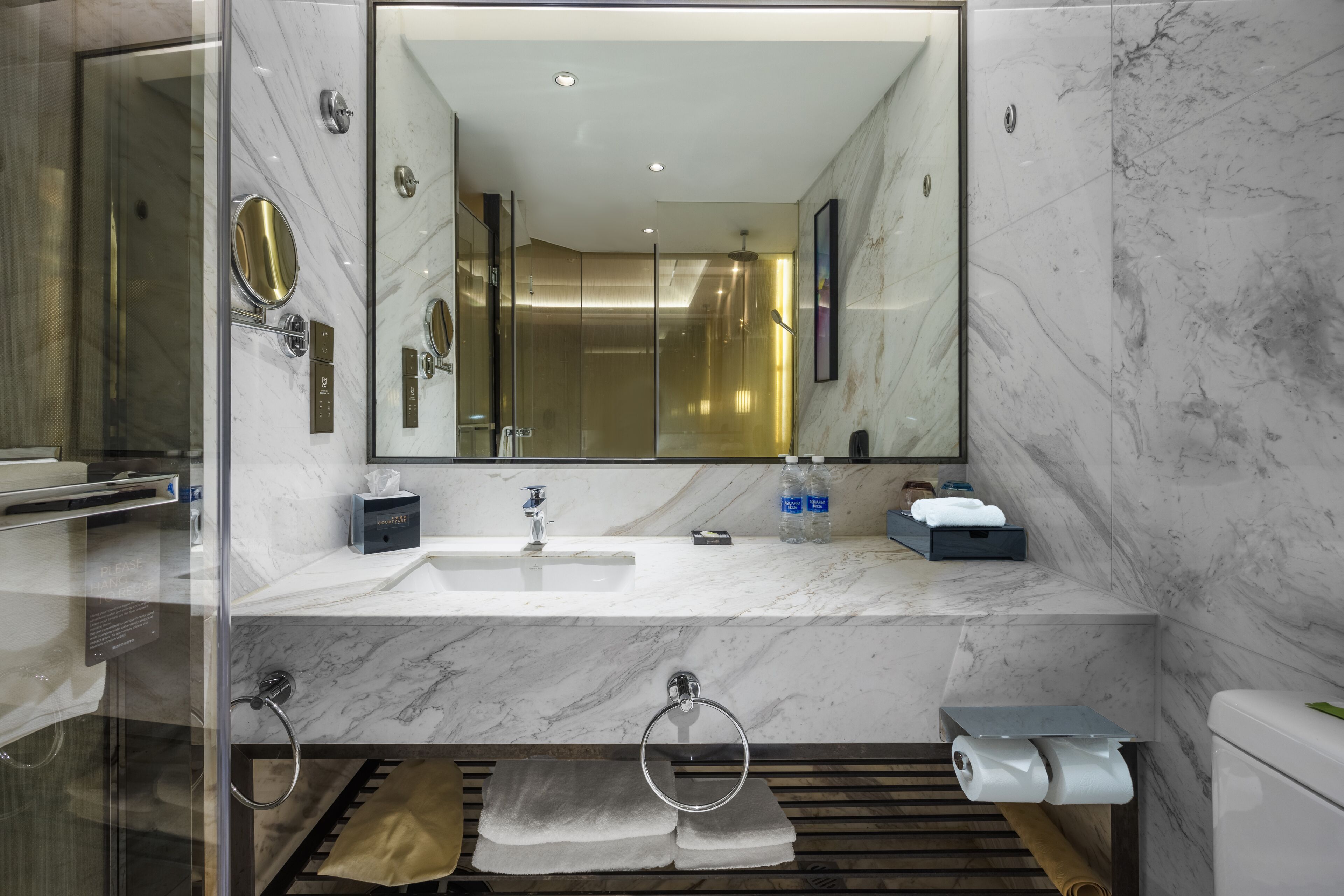A modern bathroom with a large mirror, two sinks, a toilet, and a shower area.