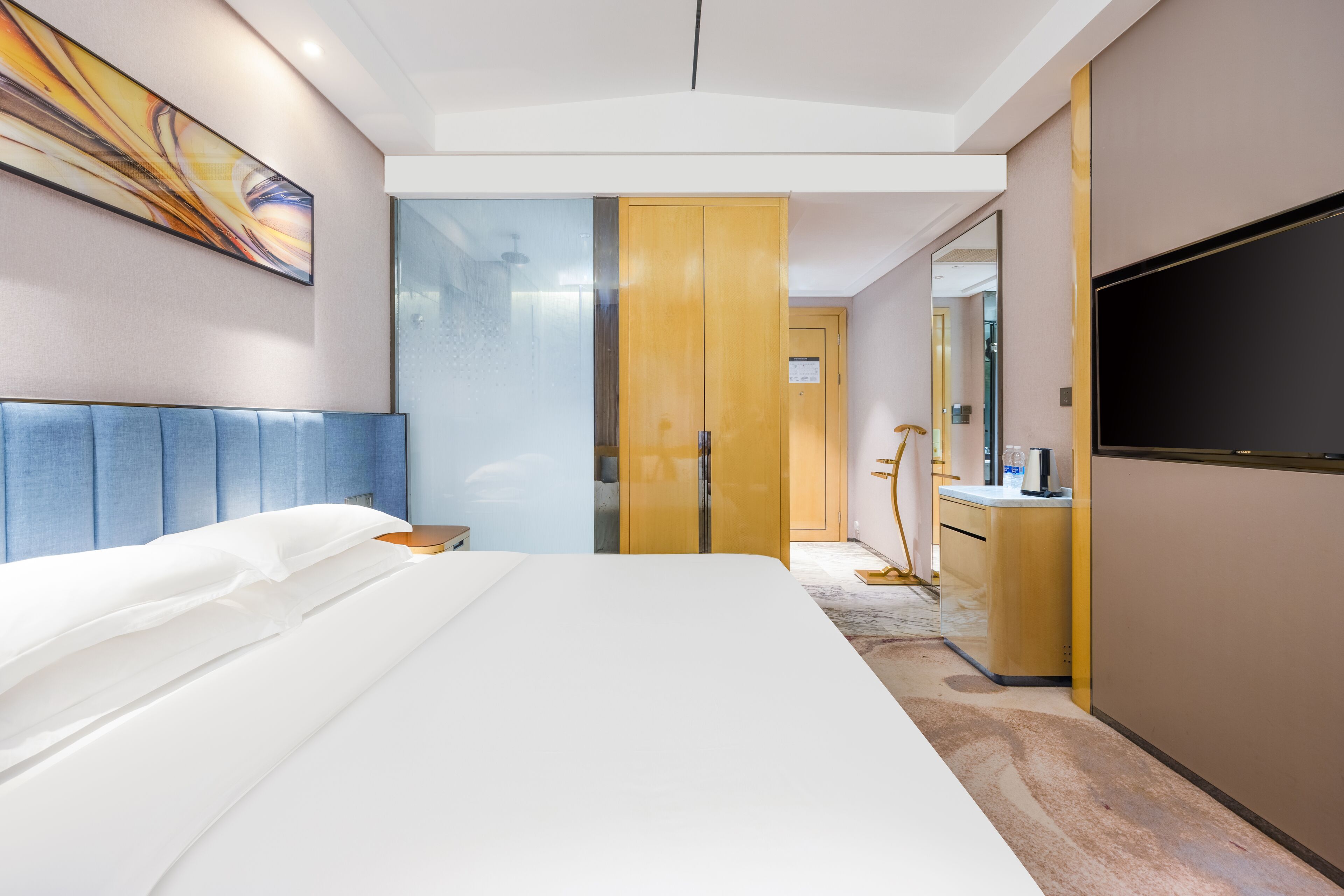A modern hotel room with a large bed, a wardrobe, a television, and a bathroom visible through a glass door.