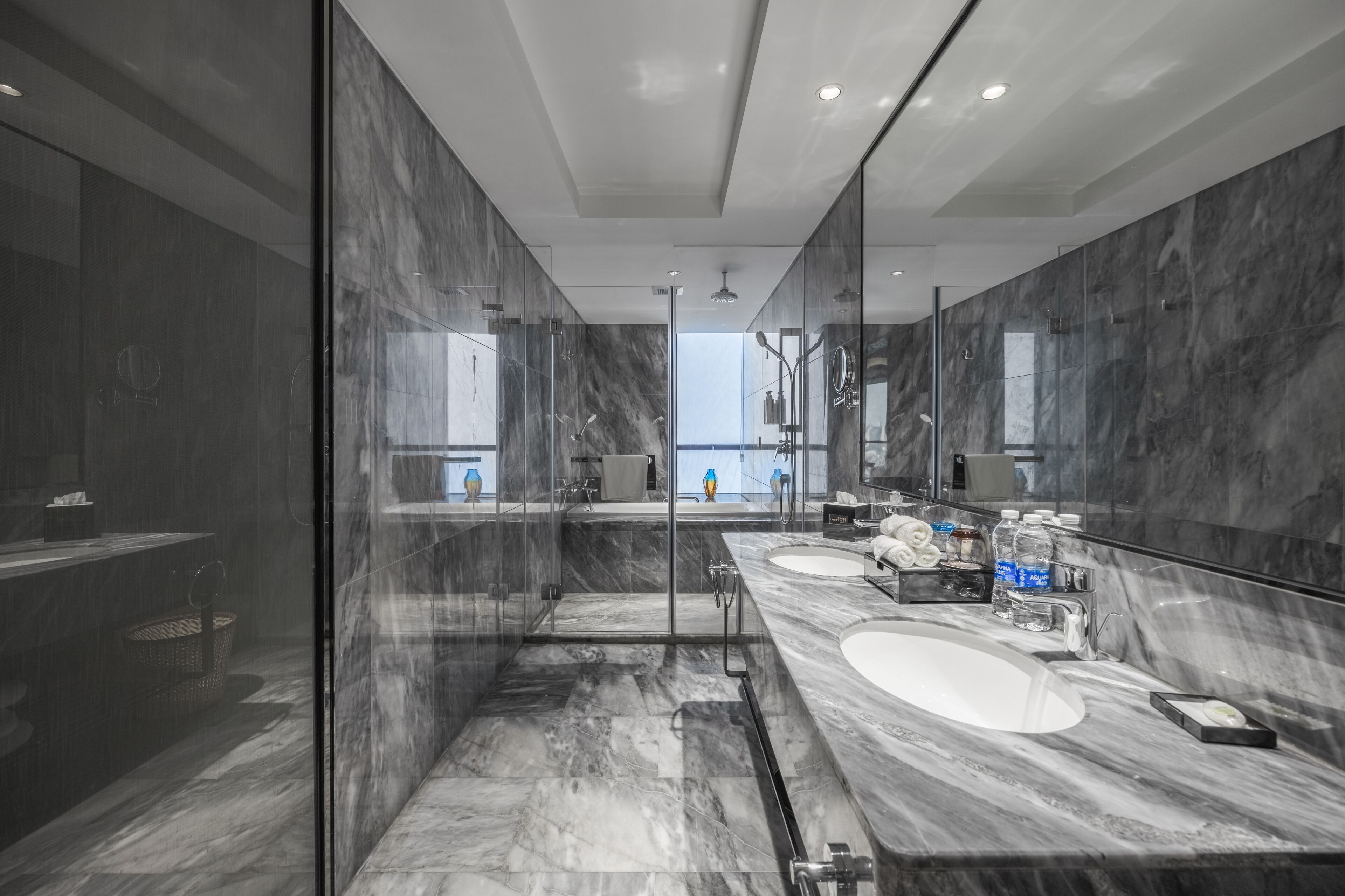 Un baño moderno con ducha de vidrio, dos lavamanos y un espejo grande.