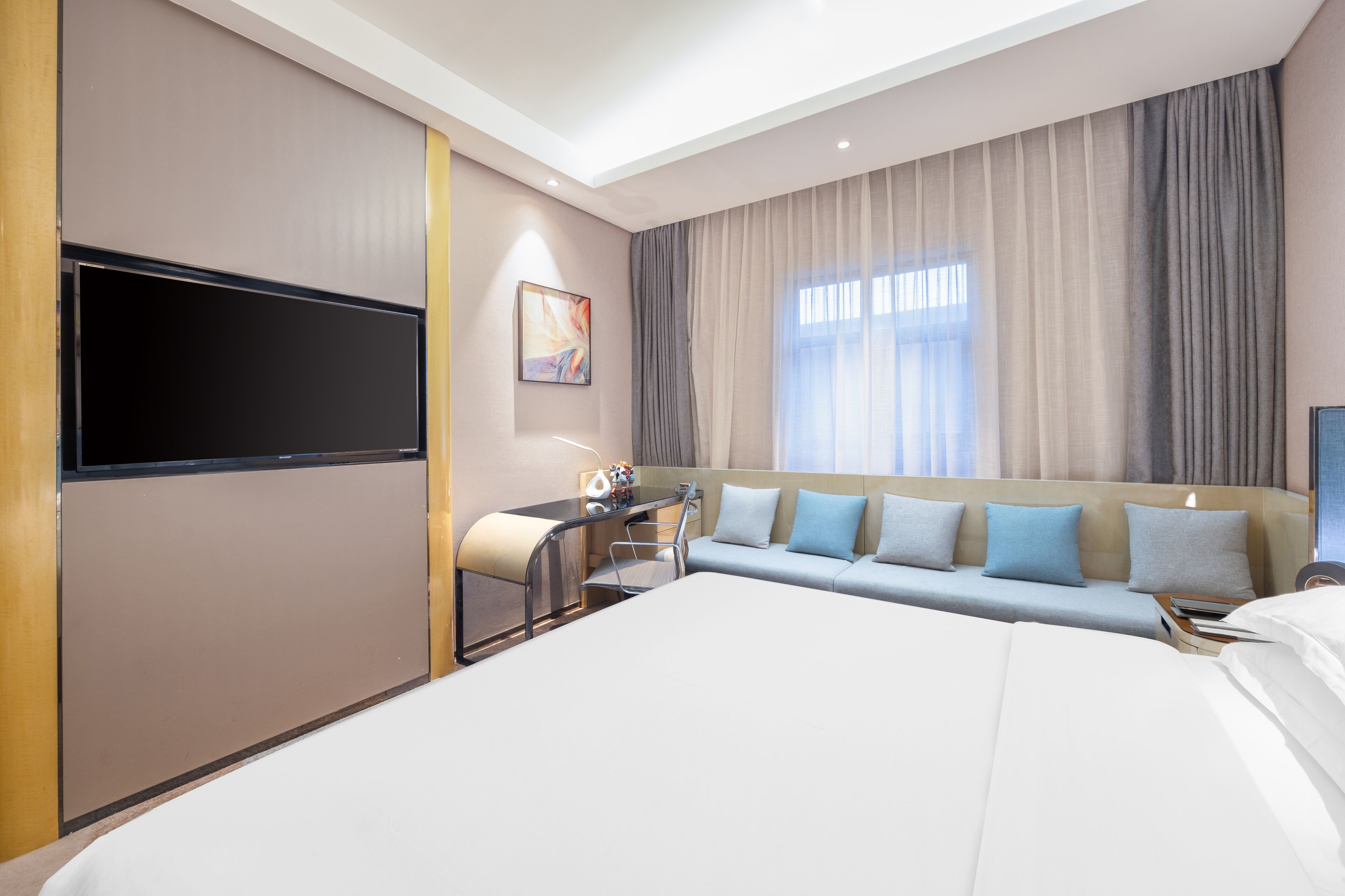 Una habitación de hotel con una cama grande, un escritorio con silla, un televisor de pantalla plana y un sofá con cojines.