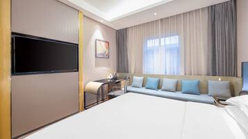 Una habitación de hotel con una cama grande, un escritorio con silla, un televisor de pantalla plana y un sofá con cojines.