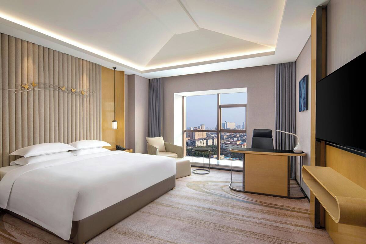 Quarto de hotel moderno com uma cama grande, uma escrivaninha, uma cadeira e uma televisão.