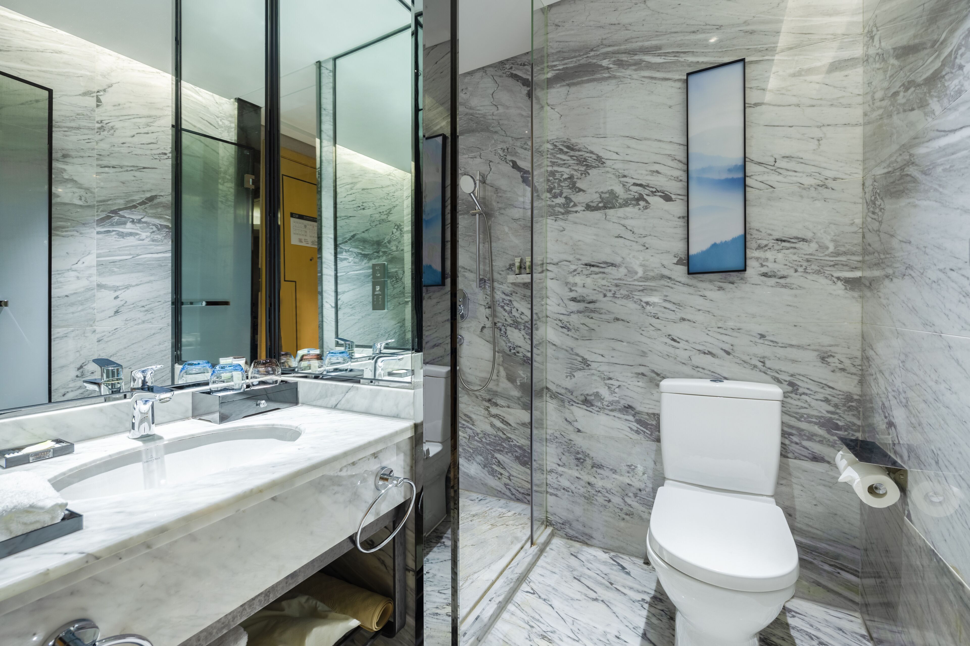 Un baño moderno con lavamanos de mármol, inodoro y ducha con mampara de vidrio.
